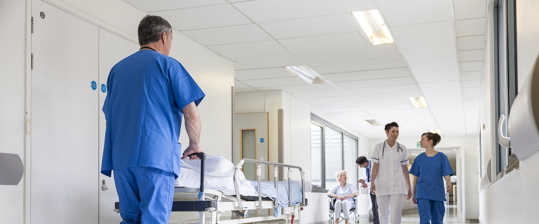 Nurse pushing trolley bed in hospital corridor)