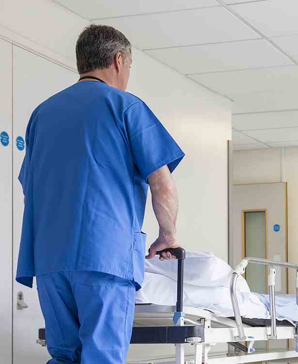 Nurse pushing trolley bed in hospital corridor)